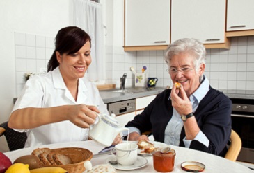 Pflegeassistenz hilft Seniorin beim Frühstück